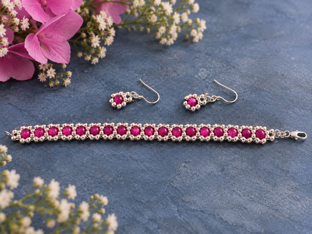 Fuchsia pink floral beaded bracelet with silver-coloured beads and matching drop earrings, laid flat on a blue background.